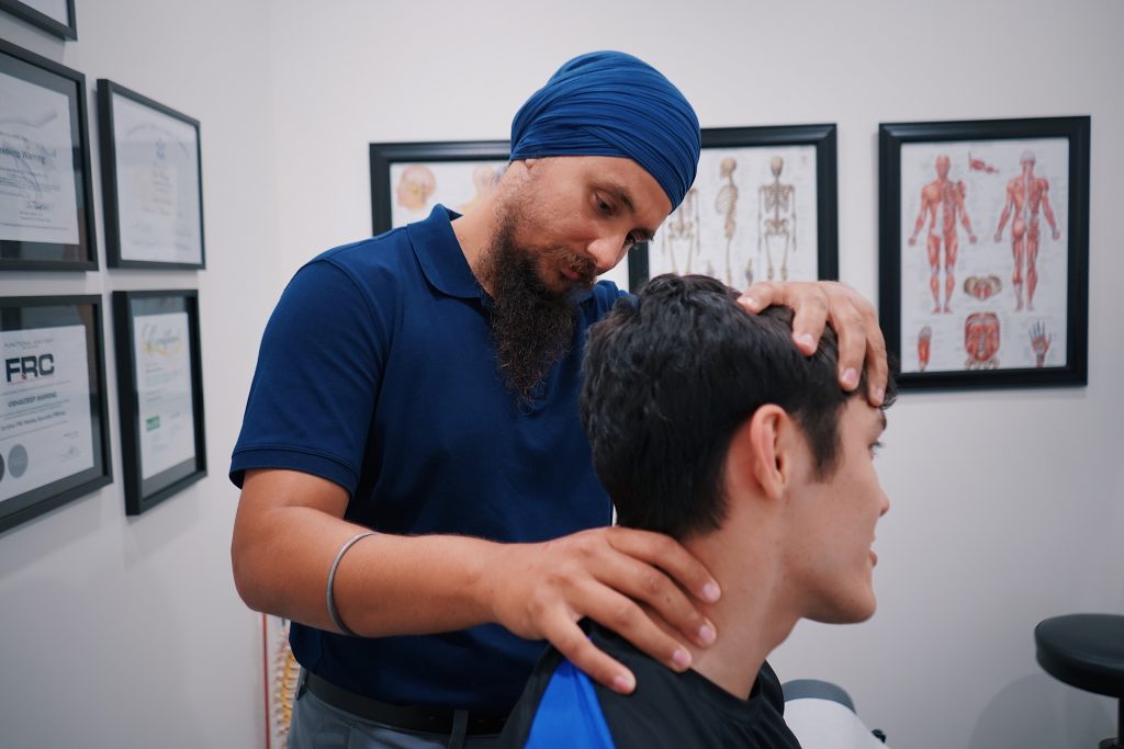 A physiotherapist is easing the neck of the patient while they're sitting down in a room full of framed pictures and charts