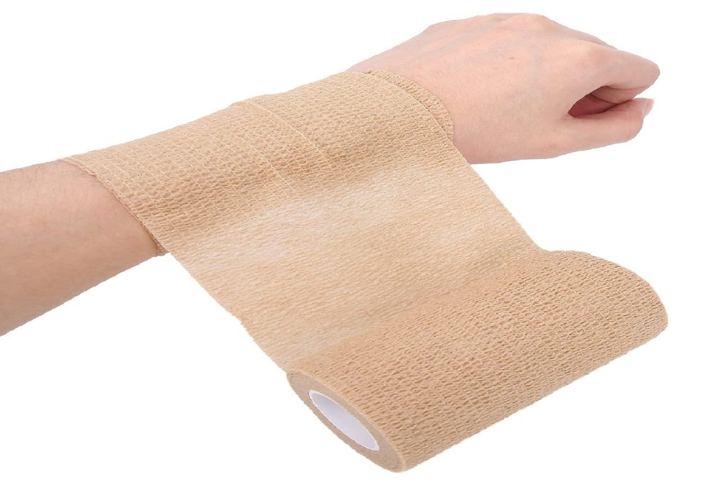 A person's arm is being wrapped with beige cohesive bandage on the wrist and around the lower forearm in front of a white background