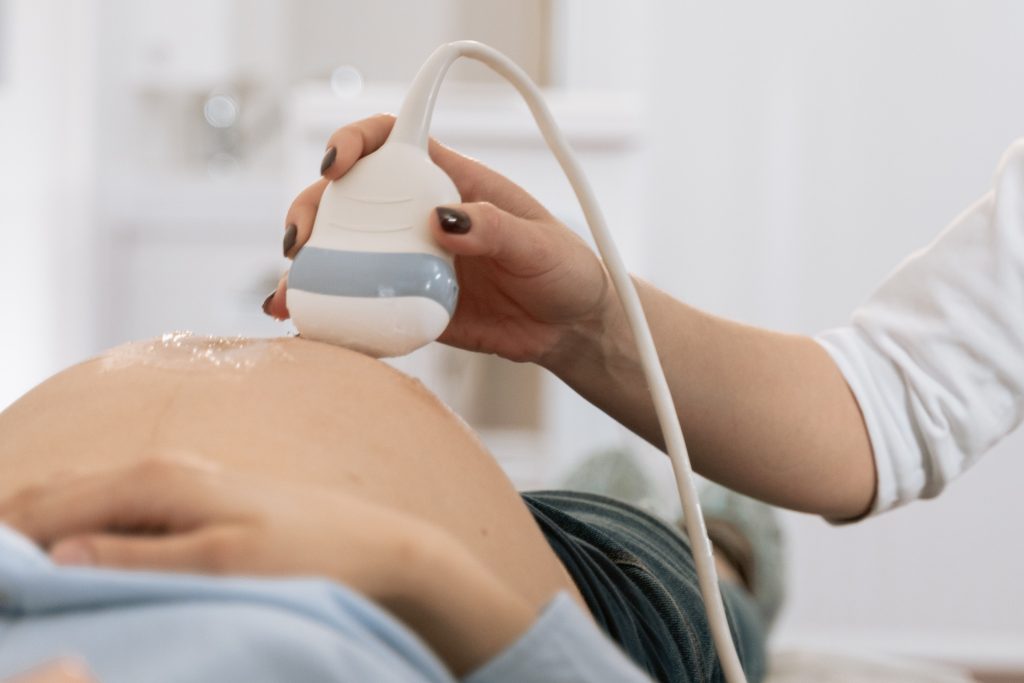 A sonographer is using a transducer with ultrasound gel on the stomach of a patient who's laying down