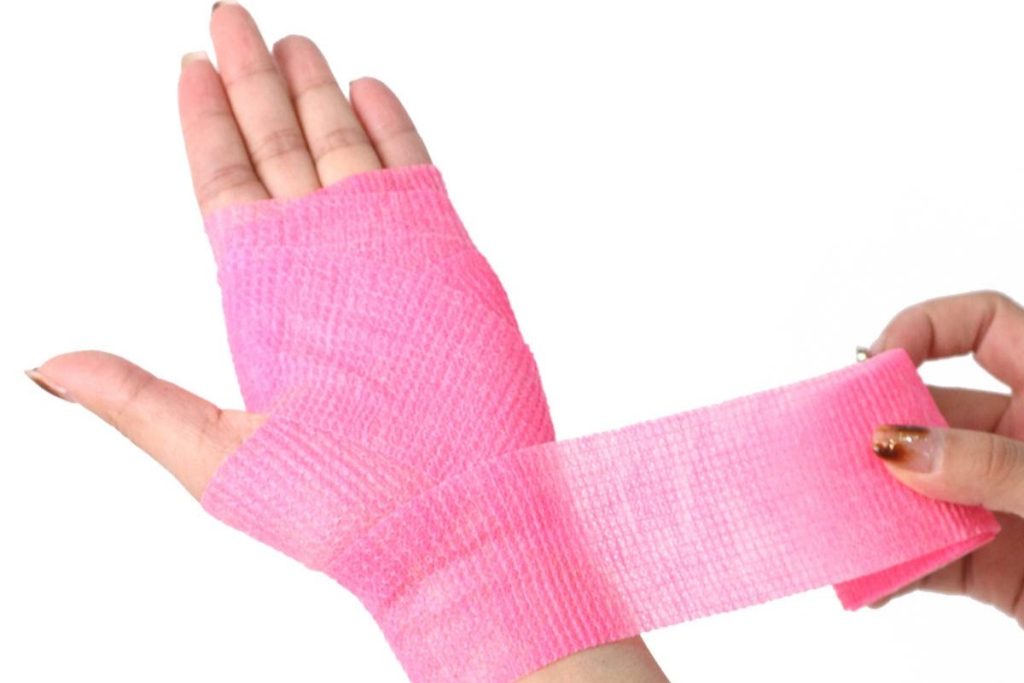 A person is using pink cohesive bandage to wrap their wrist and the palm of their hand