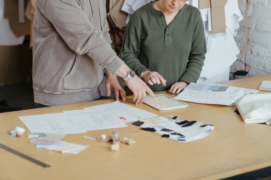 Two people wearing different shades of grey are looking over their procurement policies typed out on documents laid out on the tan table in front of them