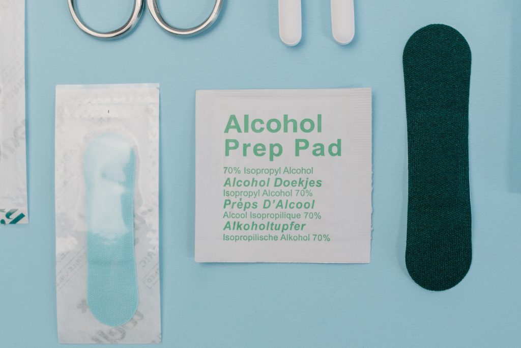 An alcohol prep pad is on a light blue table, surrounded by other materials such as bandages and part of a pair of scissors