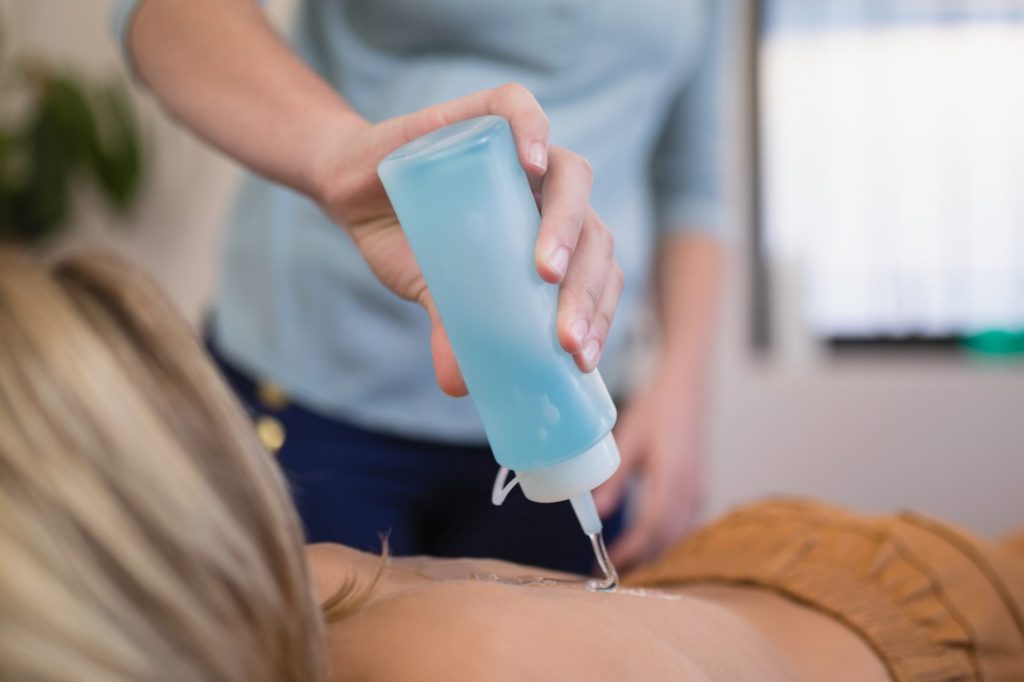 A medical practitioner is putting the blue ultrasound gel on the stomach of a patient while they're laying down