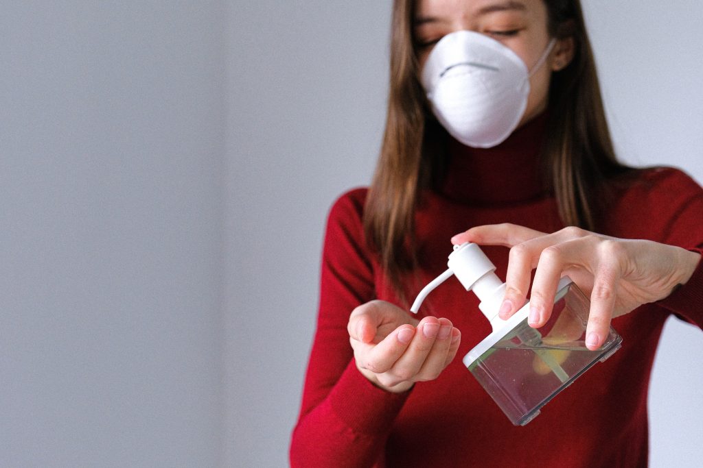 A woman wearing a red turtleneck sweater is putting hand sanitiser with some disinfectant or antiseptic in it on her hand using a clear bottle with a pump cap