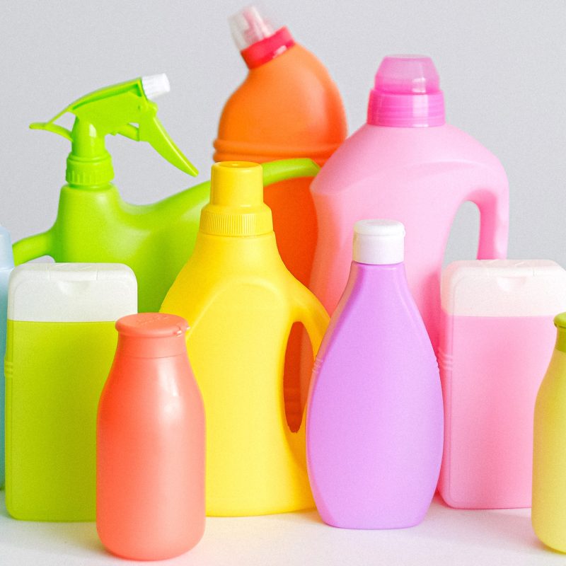 Different-sized and different-coloured bottles of disinfectants and antiseptics are arranged on a white table while in front of a white background