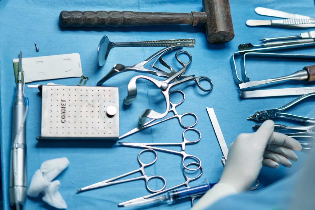 A mix of medical equipment like surgical tools like carmalt forceps on a bed of blue sterilised cloth on a separate surgical table