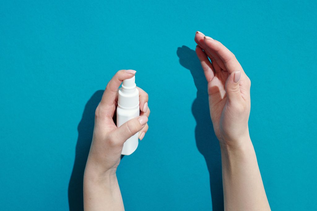 A pair of hands in front of a blue background is spraying on an antiseptic first aid spray called chlorhexidine