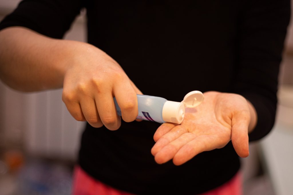 A person wearing a black long-sleeved shirt while pouring some antimicrobial dye on their hands