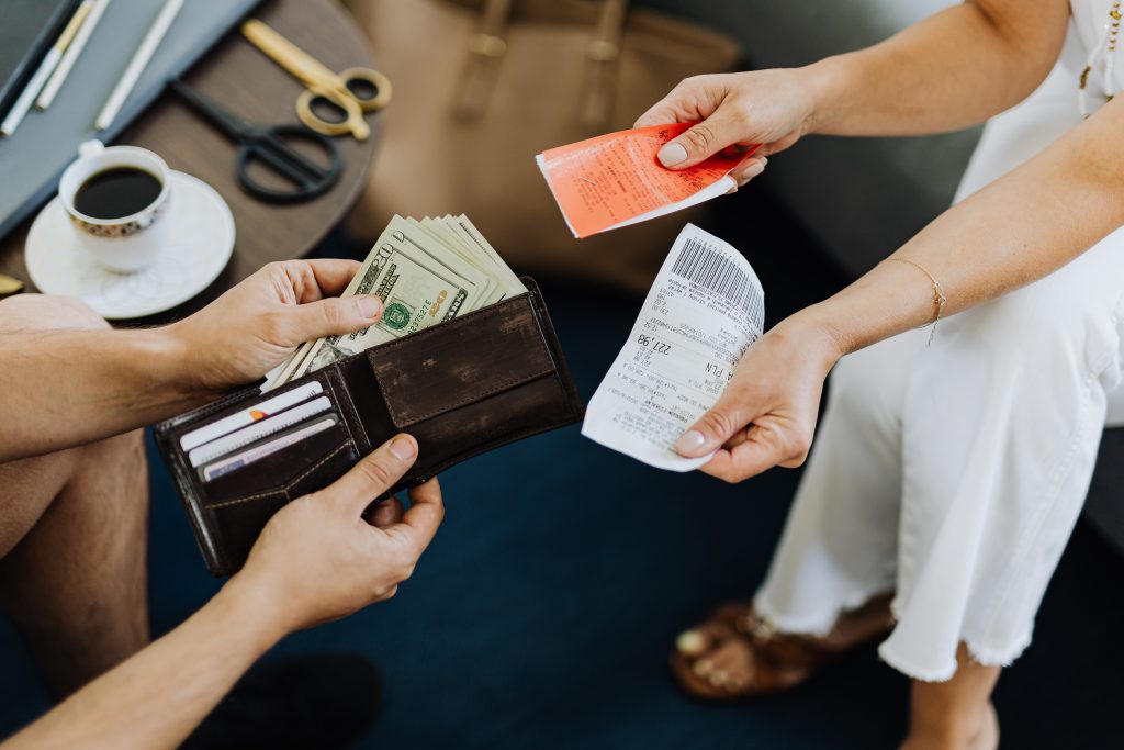 A person is showing the money in their pocket while sitting down, using the money to pay for the clinic supply bill in the other person's hand