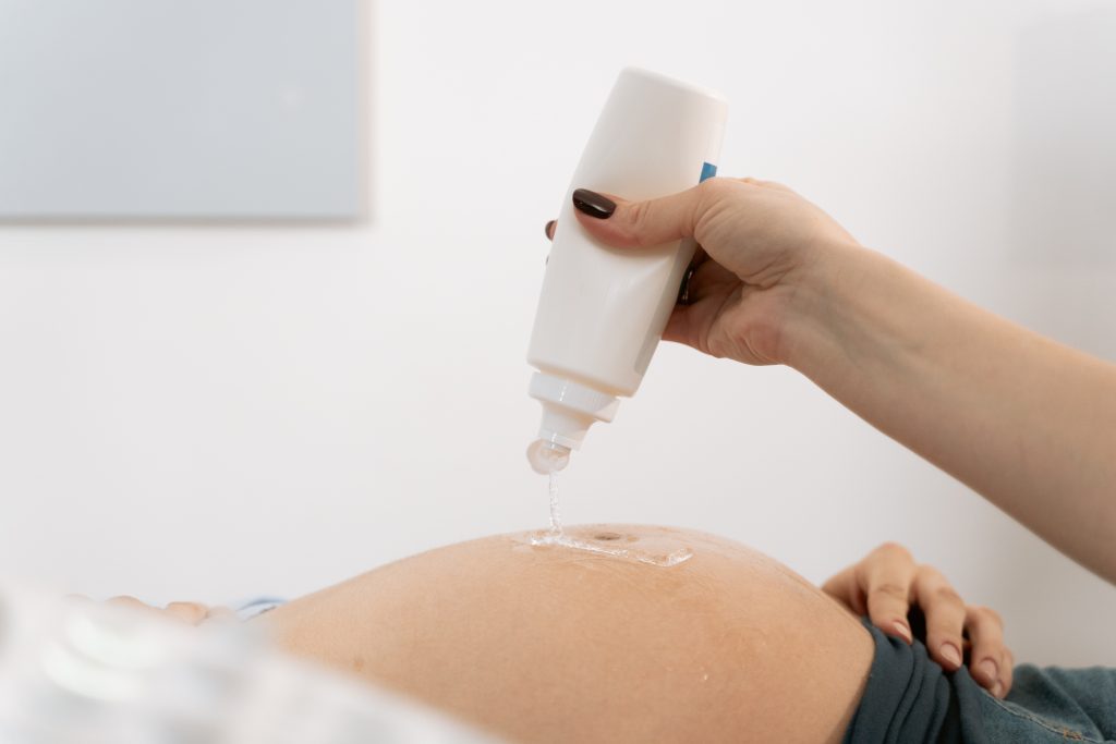 A medical professional is squirting on ultrasound gel using a white bottle on the belly of a patient
