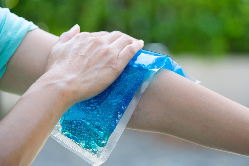 A person is using their hand to put the cold pack on their elbow while wearing a blue shirt