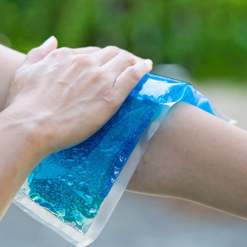 A person is using their hand to put the cold pack on their elbow while wearing a blue shirt