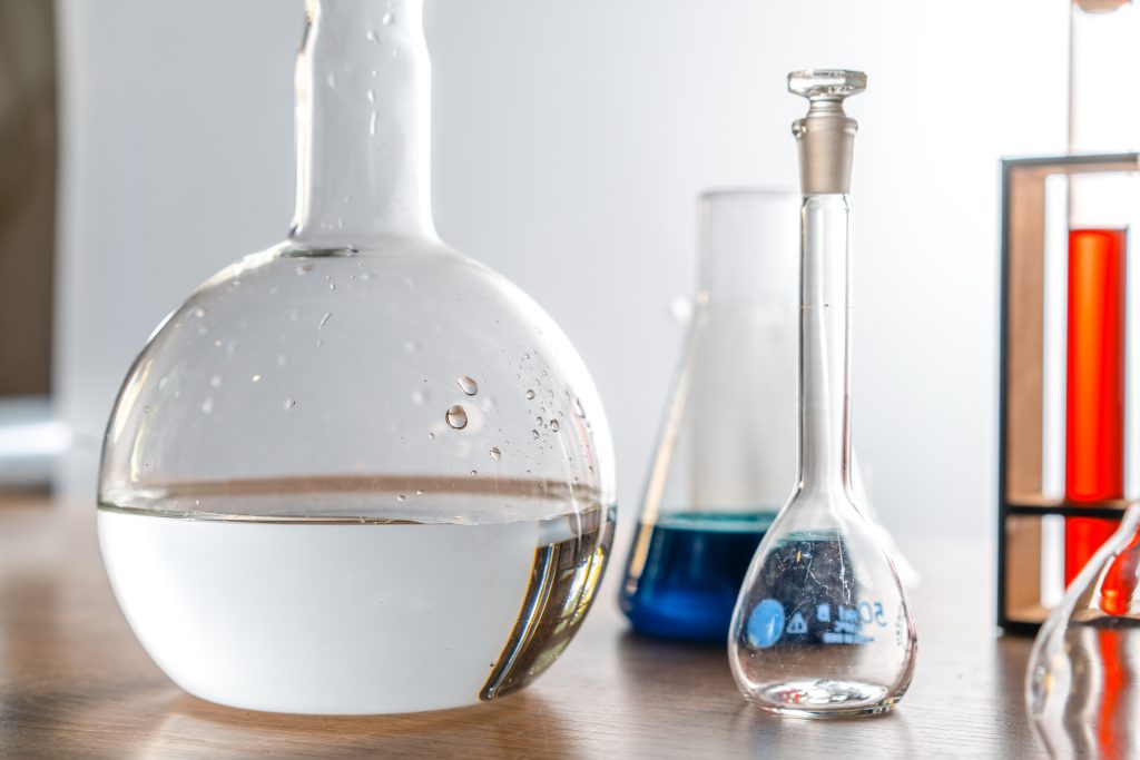 A florence flask of distilled water is on a table along with other chemistry glassware filled with other liquids