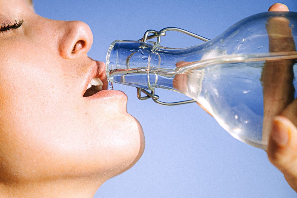 A person in front of a light blue background is drinking distilled water from a glass bottle