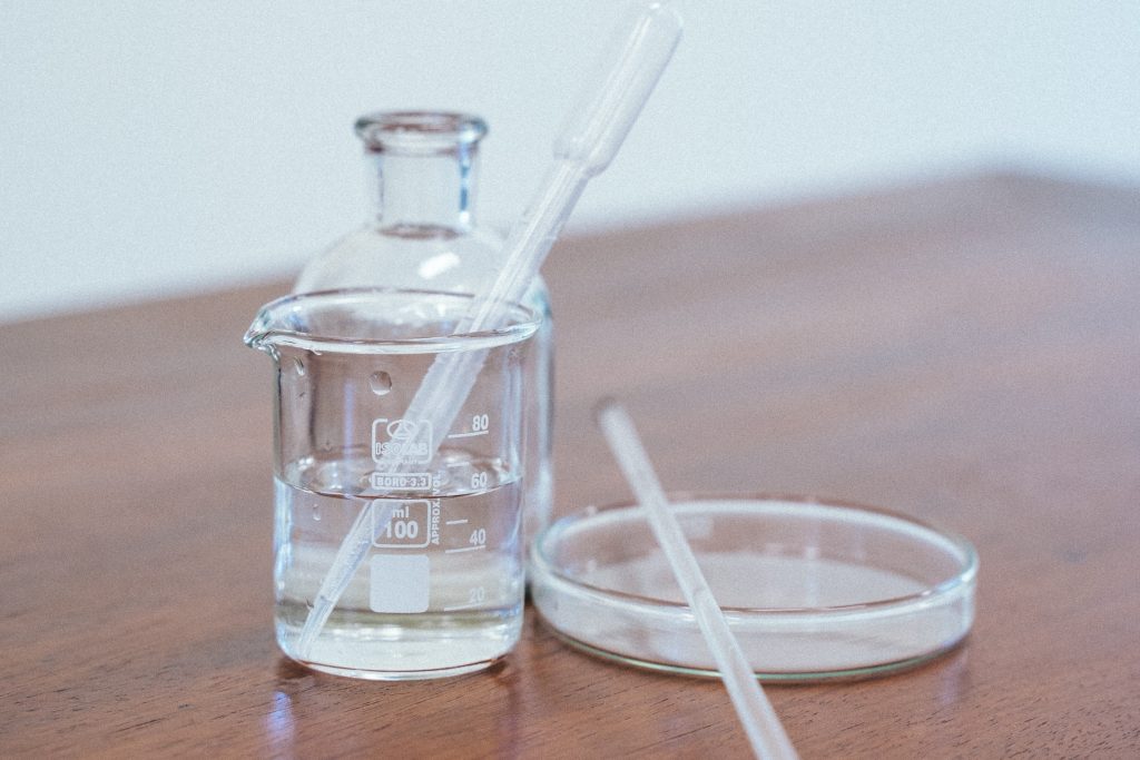 A beaker is full of distilled water and other chemistry glassware is on the table while there is a white background