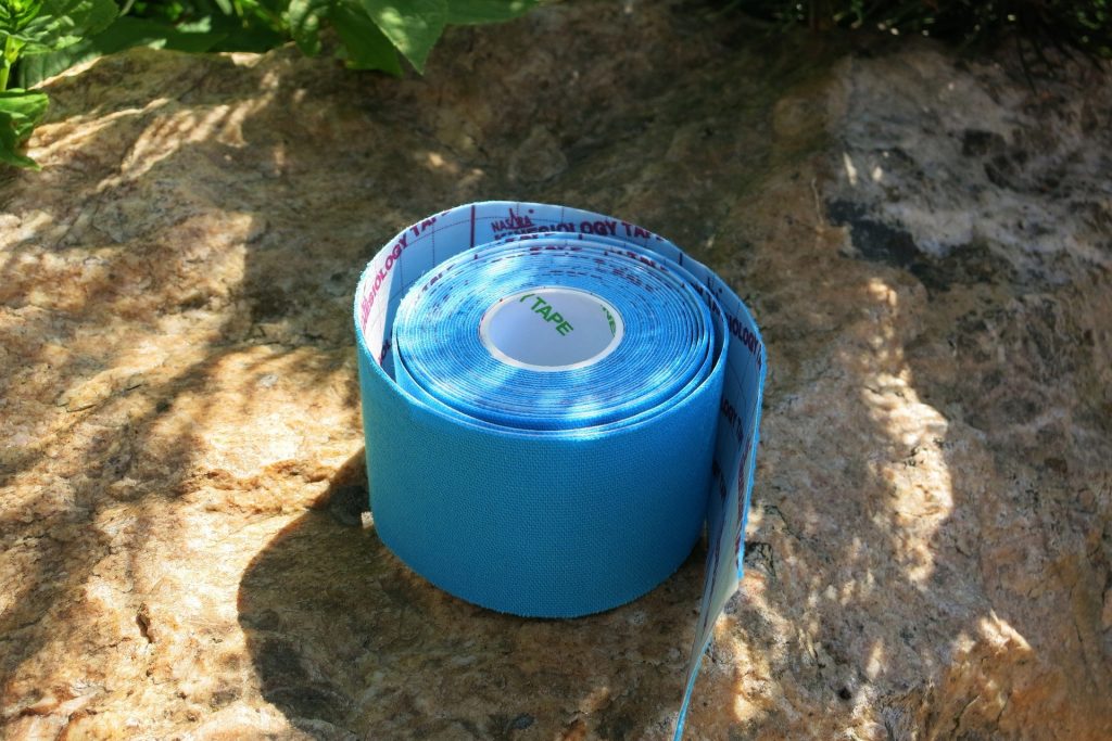 A roll of blue sports medicine tape is put on top of a rock with a bit of sunlight on it while the tape is outside surrounded by a few plants