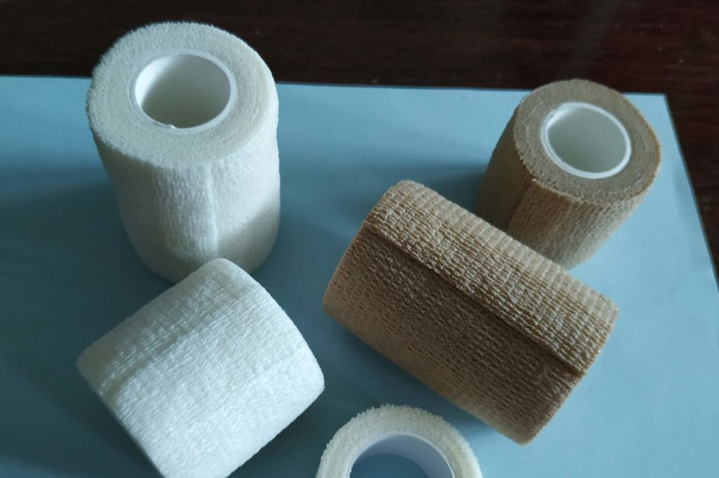 Rolls of tan/brown and white sports medicine tape is put on top of a light blue table