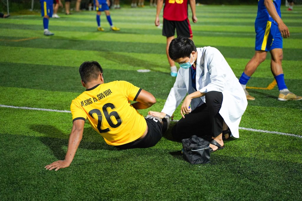 A rugby player is sitting up on the rugby field during a game while a physiotherapist check their leg for injuries