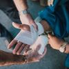 A close-up photo of two pairs of hands. The pair of hands on the left is providing first aid by bandaging an outstretched right hand on the right side of the image.