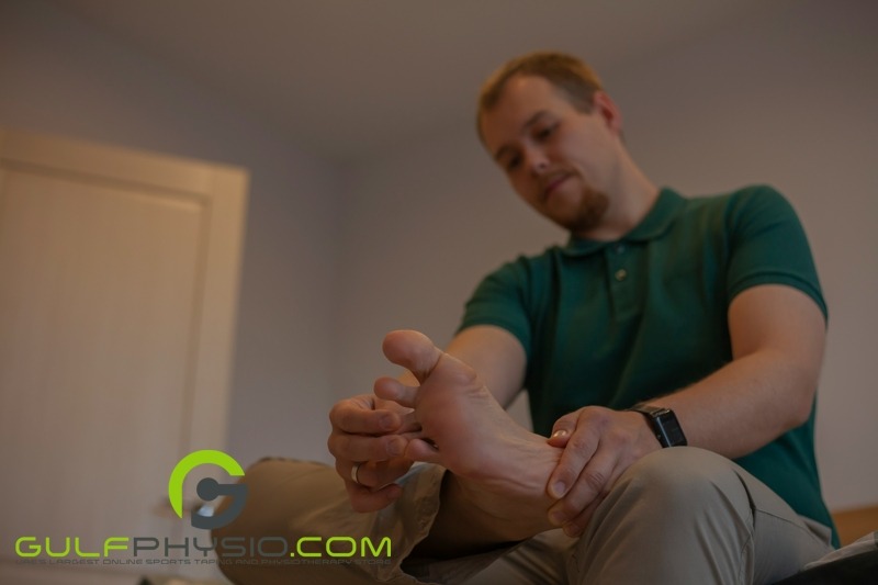 A man is sitting down and massaging his foot.