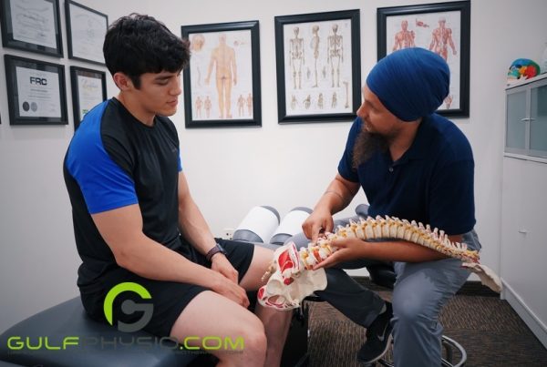 A medical practitioner holds a model of the human spine while explaining a diagnosis to the patient.